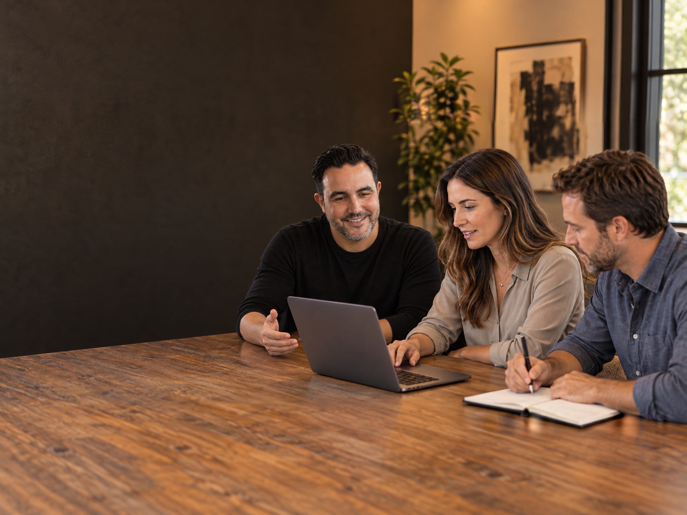 A rendered scene of a working session: a facilitator and two team members at a table, working from a laptop and a notebook.
